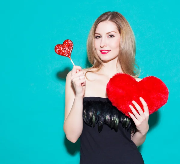 Fashionable beautiful girl holding a red candy heart and big toy heart. In a black dress on a green background in the studio. Look at the camera. Fashion Beauty Girl. Gorgeous Woman Portrait. Sexy Gla — 图库照片