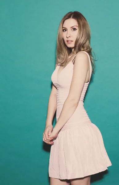 Menina assustada, de pé em um vestido curto rosa posando em um fundo verde no estúdio. Tonificado — Fotografia de Stock