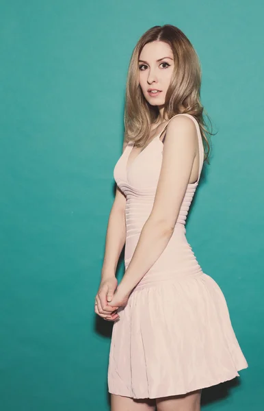 Frightened girl, standing in a short pink dress posing on a green background in the studio. Toned — Stock Photo, Image