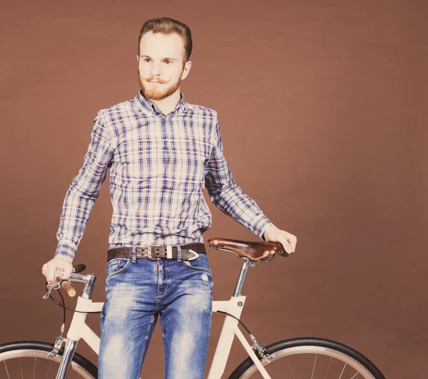 Un jeune homme avec la moustache et la barbe est à proximité du vélo fixgear moderne à la mode. Jeans et chemise à carreaux style hipster. Couleur tonique — Photo