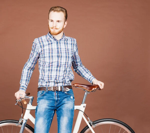 Młody człowiek z wąsy i brodę znajduje się w pobliżu modne nowoczesne fixgear rowerów. Dżinsy i plaid shirt hipster stylu. Stonowanych kolorów — Zdjęcie stockowe