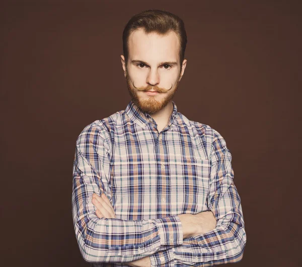 Portrait of a young man with a mustache and beard jeans and plaid shirt hipster style in the studio. Toned color. Indoor — Stock Photo, Image