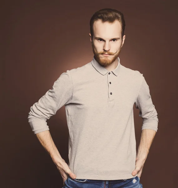 Πορτρέτο ενός νεαρού άνδρα με μουστάκι και γένια τζιν και πουκάμισο στυλ hipster στο στούντιο. Εσωτερική, τονισμένο χρώμα. — Φωτογραφία Αρχείου