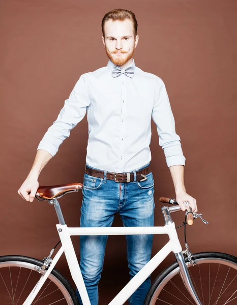 Un jeune homme avec la moustache et la barbe est à proximité du vélo fixgear moderne à la mode. Jeans et chemise, le style hipster du nœud papillon. Couleur tonique — Photo