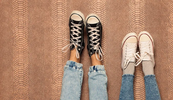 Jovens pernas de casal de moda em jeans e tênis pés para cima na parede. Fecha. No interior. Cor quente . — Fotografia de Stock