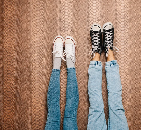 Jovens pernas de casal de moda em jeans e tênis pés para cima na parede. Fecha. No interior. Cor quente — Fotografia de Stock