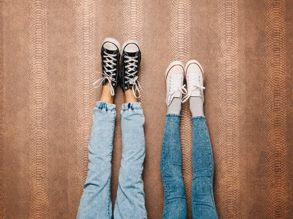Jovens pernas de casal de moda em jeans e tênis pés para cima na parede. No interior. Cor quente — Fotografia de Stock