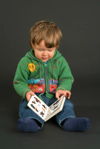 Ung pojke sitter och ser en bok — Stockfoto