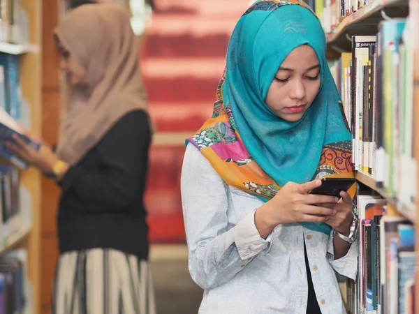 En kvinnlig student med en telefon i ett bibliotek — Stockfoto