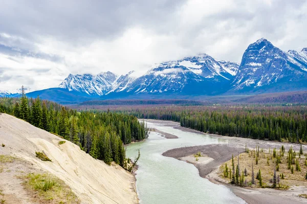 Forested valley and river near mountains under low clouds, at Athabasca River, Alberta, Canada.