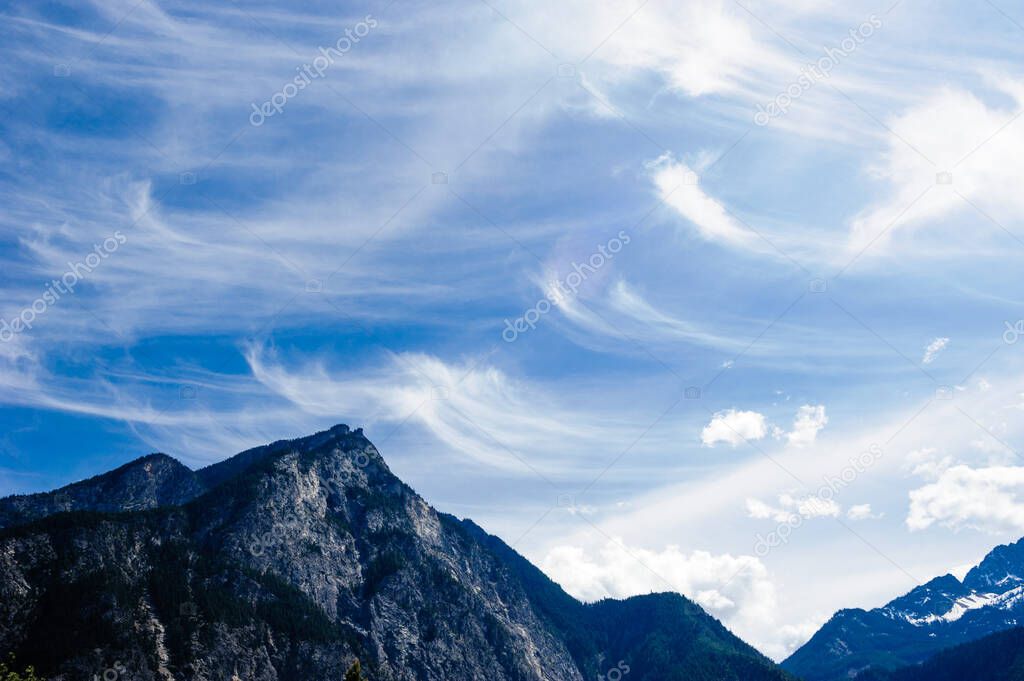 Cirrus clouds spreading into curved patterns above mountains in British Columbia, Canada.