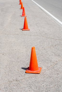 Asfalttaki beyaz doğruya paralel turuncu trafik konileri sırası.