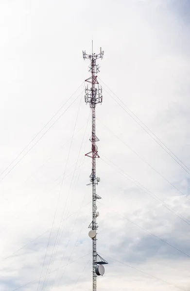 高耸的红色和白色金属通信天线塔 配有天线盘和辅助电缆 与多云的灰色天空抗衡 — 图库照片