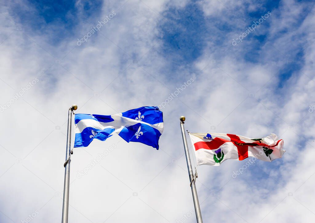 Flags of Quebec and Montreal flapping in wind against sky with clouds.