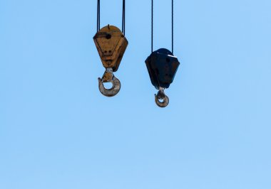 Pair of hanging industrial crane hoists on pale blue sky. clipart