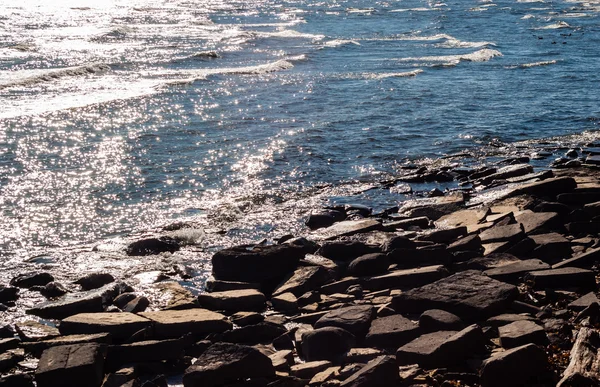 Kahverengi kayalık sahil ve güneş ışığı yansıtan su. — Stok fotoğraf