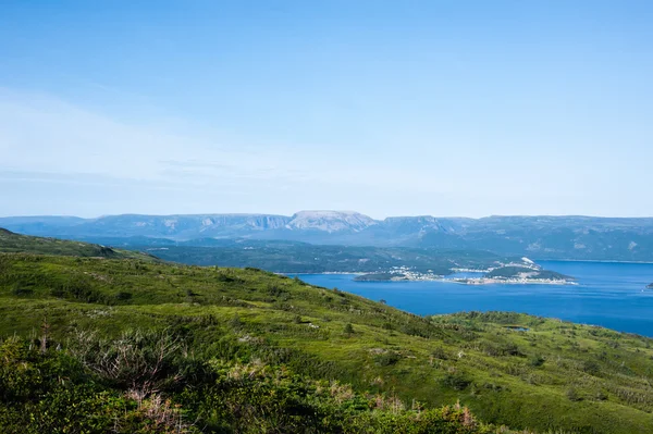 Colinas verdes cerca del agua contra la meseta bajo el cielo azul pálido —  Fotos de Stock