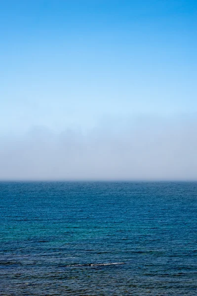 Sis mavi gökyüzü altında dalgalı su üzerinde düşük — Stok fotoğraf