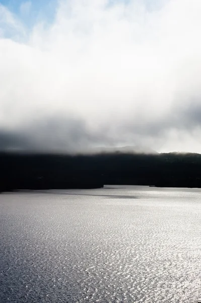 Nebelschwaden über dunkler Küste und beleuchtetes Wasser — Stockfoto