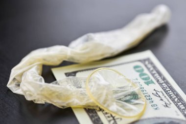 Used condom and US dollars bills. Cum in condom. Prostitution concept. Pay for sex per night. Harlotry and whoredom. US dollar money on table with contraceptive.