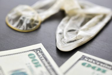 Used condom and US dollars bills. Cum in condom. Prostitution concept. Pay for sex per night. Harlotry and whoredom. US dollar money on table with contraceptive.