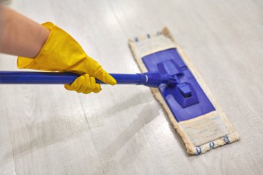 Koruyucu sarı lastik eldivenli genç bir kadın evde yerleri temizlerken ıslak bez kullanıyor..