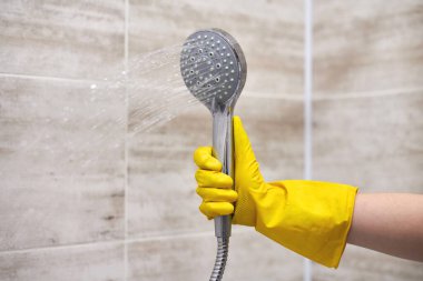 Koruyucu kauçuk eldivenli kadın duş başlığını ev banyosuna dökülen suyla tutuyor, kopyalama alanı, hareket bulanıklığı.