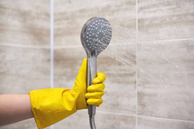 Koruyucu kauçuk eldivenli kadın duş başlığını ev banyosuna dökülen suyla tutuyor, kopyalama alanı, hareket bulanıklığı.