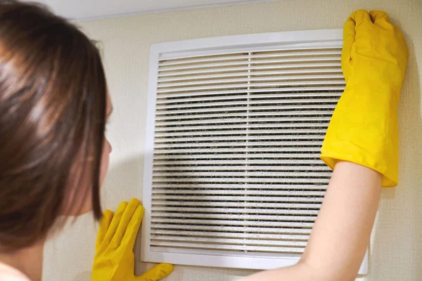 Hands in protective rubber gloves opening clogged air ventilation grill of HVAC with dusty filter to clean or replace it. Cleaning service concept.