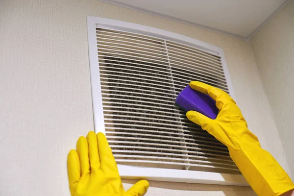 Hands in protective rubber gloves cleaning dusty air ventilation grill of HVAC. Cleaning service concept.