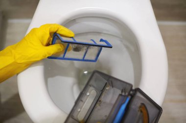 Elleri koruyucu lastik eldivenlerle tuvaletteki robot süpürge filtresinden çöp atıyor. Tıkanmış kaseyi önlemek için tuvalete çöp ve yabancı nesneler atmayın. Kapat..