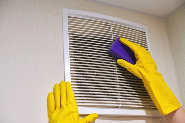 Hands in protective rubber gloves cleaning dusty air ventilation grill of HVAC. Cleaning service concept.