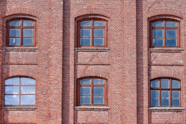 6 arched glass windows set in red brick wall. Vintage windows in brown wooden frames on red brick wall of industrial building.