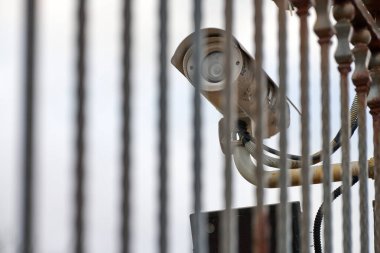 IP güvenlik kamerası ve gri gökyüzü arka planında demir çit, şehir manzarası. Korunaklı bölge, sanayi bölgesi.