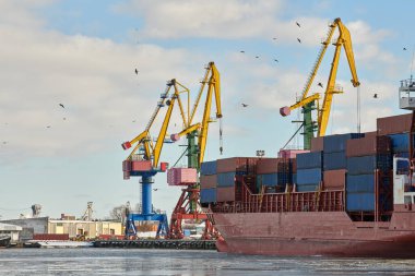 Limanda demirli kargo gemileri ve vinçler var. Liman, kargo konteynır alanı, konteyner gemisi terminali, tersane. İş ve ticaret, lojistik. Kış sanayi sahnesi.