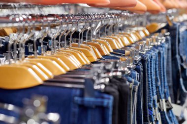 Dükkandaki ahşap askılarda asılı mavi ve siyah kotlar. Askıda bir sürü kot pantolon asılı. Dolapta asılı pantolon pantolonu. Alım, satım, alışveriş ve kot pantolon modası kavramı.