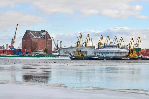 Moored cargo ships and harbor cranes in port. Seaport, cargo container yard, container ship terminal, shipyard. Business and commerce, logistics. Winter industrial scene.