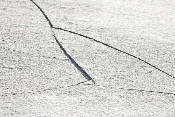 Cracked ice of frozen lake with white snow on top. Ice texture background, close up.