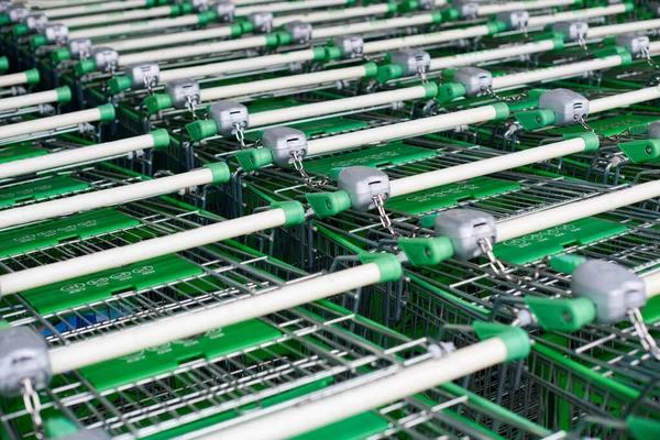 Row of parked trolleys in supermarket. Many empty green shopping carts in row.