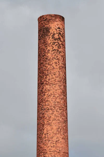 Old brick factory pipe on grey sky background. Pollution of environment, ecology and industrial, emissions into water resources, oncological diseases, cancer concept.