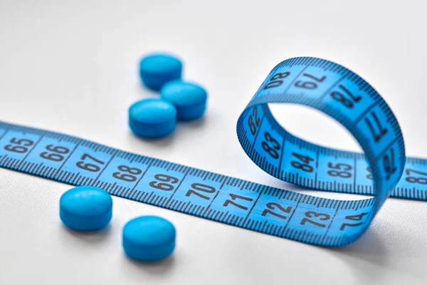 Blue round diet pills and measuring centimeter tape isolated on white background. Diet, slimming, weight loss concept.
