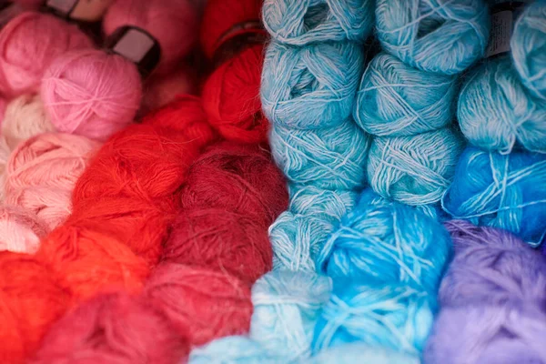 Yarns or balls of wool on shelves in store for knitting and needlework, close up. Accessories for haberdashery in fabric store shelves. Multicolored picture, background.