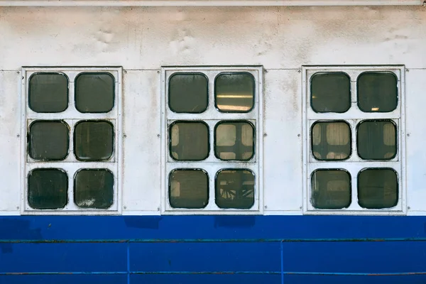 Cabin windows and portholes on outboard side of ship. Close up of hull of vintage ocean liner. Old ship cabin windows, white and blue wall.