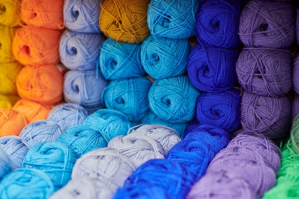 Yarns or balls of wool on shelves in store for knitting and needlework, close up. Accessories for haberdashery in fabric store shelves. Multicolored picture, background.