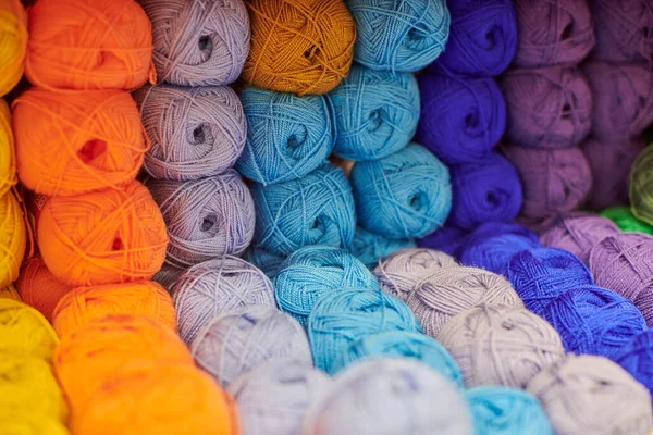 Yarns or balls of wool on shelves in store for knitting and needlework, close up. Accessories for haberdashery in fabric store shelves. Multicolored picture, background.