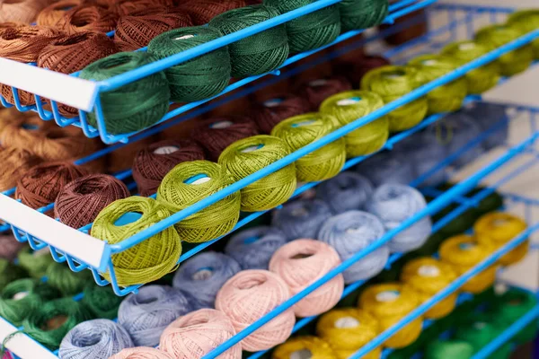 Yarns or balls of wool on shelves in store for knitting and needlework. Accessories for haberdashery in fabric store shelves. Multicolored picture, background.