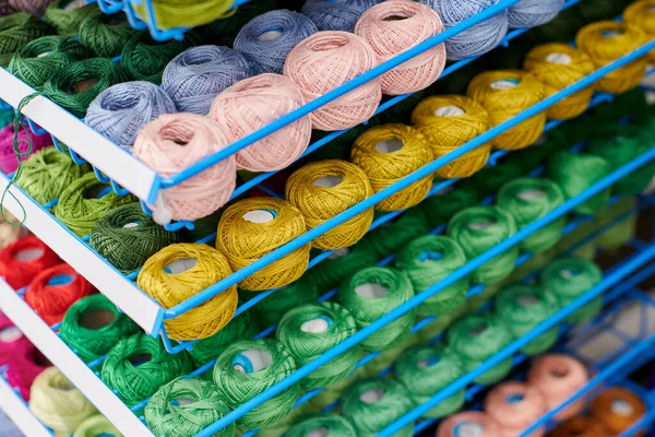 Yarns or balls of wool on shelves in store for knitting and needlework. Accessories for haberdashery in fabric store shelves. Multicolored picture, background.