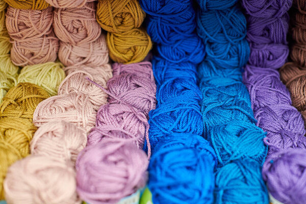 Yarns or balls of wool on shelves in store for knitting and needlework, close up. Accessories for haberdashery in fabric store shelves. Multicolored picture, background.
