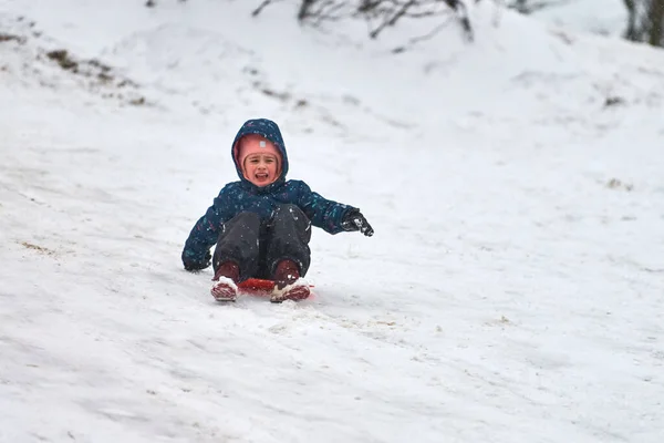 モスクワ 2021 青いダウンジャケットの陽気な女の子が赤いそりで丘を転がっています 冬のスポーツ活動 — ストック写真