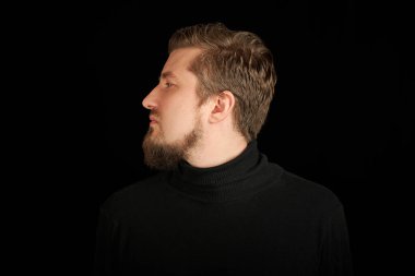 Sevimli sakallı adam, yarı yüz portresi, siyah arka plan. Siyah polo yakalı genç adam. Kendinden emin, başarılı bir adam..
